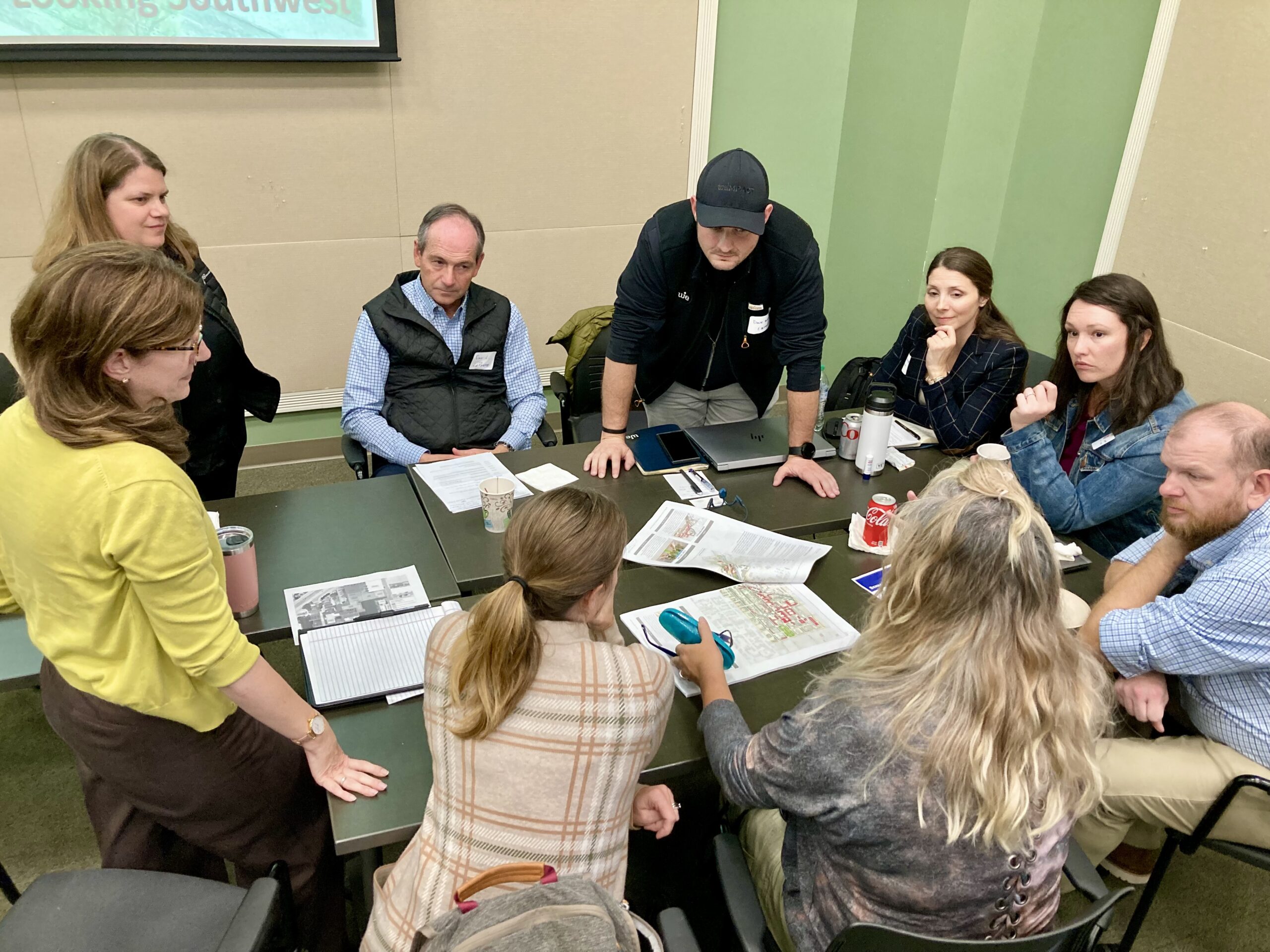 A group of architects, planners, city staff, and developers huddle around a table during a charrette implementation workshop.